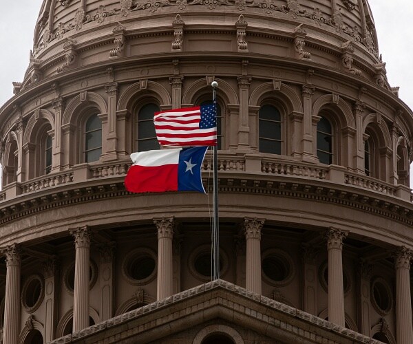 american and texas flags fly on texas state capitol building