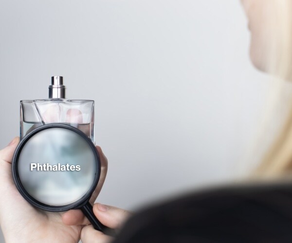 woman holds perfume bottle, label on it indicates there are phthalates in it