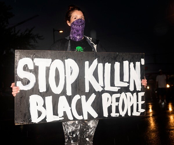 a white woman in a bandana holds a sign that says stop killin' black people