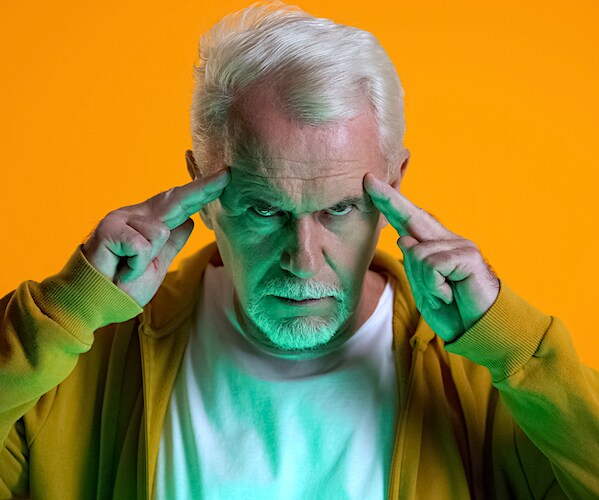 an elderly man points his fingers to his temples