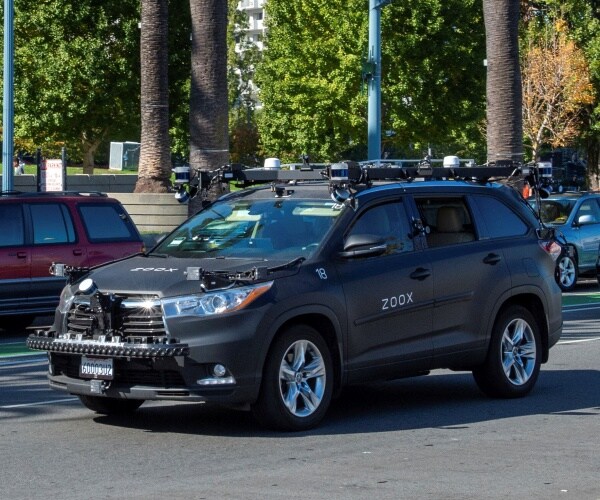 dark gray car with zoox labeling on the side driving in a parking lot