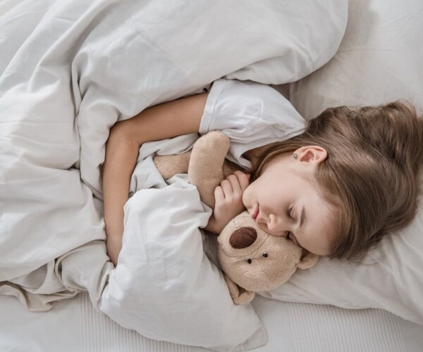 young girl with stuffed animal asleep under weighted blanket