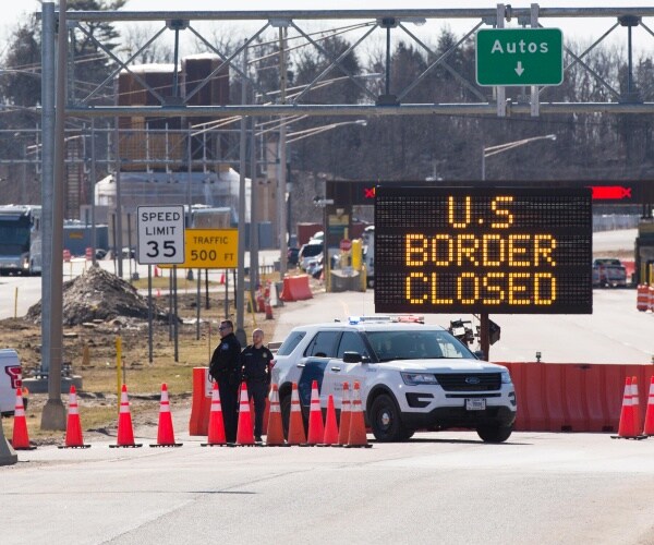 U.S. Customs officers stand beside a sign saying that the U.S. border is closed.