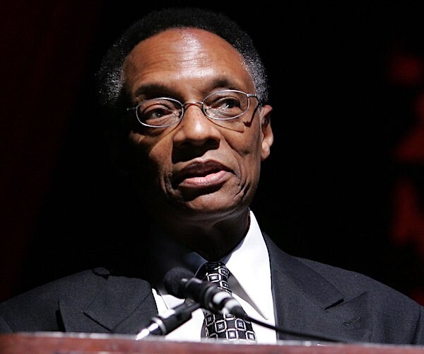 ramsey lewis stands on a dark stage during a speech