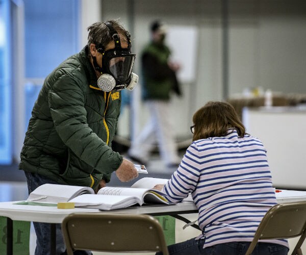 a voter awaits a poll worker as the stands by in full mask and green jacket