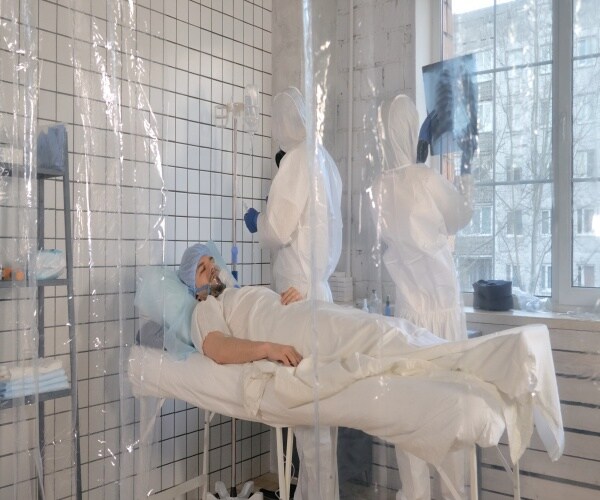 Man in hospital bed with doctors in protective gear