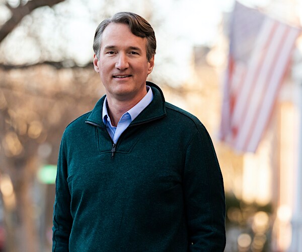 glenn youngkin stands outdoors with an american flag in the background