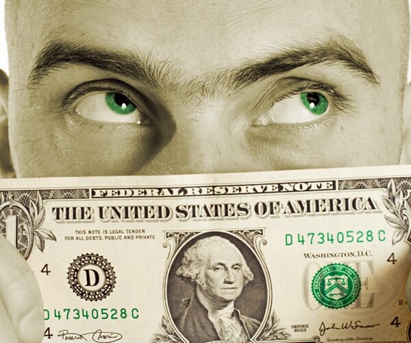 man holds a US one dollar bill to his face obsesessed with a fantasy of more money.