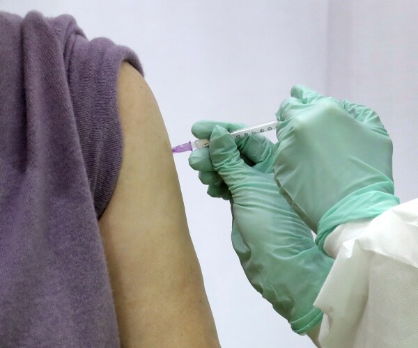 nurse with syringe and green gloves gives woman in a purple top a shot