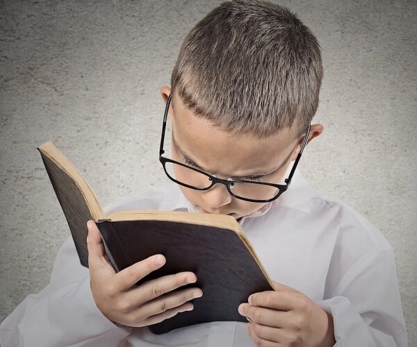 young boy wearing glasses looking closely at book