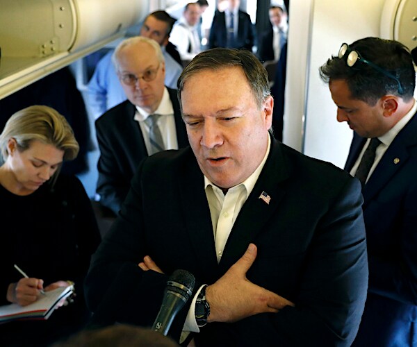 secretary of state mike pompeo folds his arms with his hands in his armpits while answering questions aboard a plane