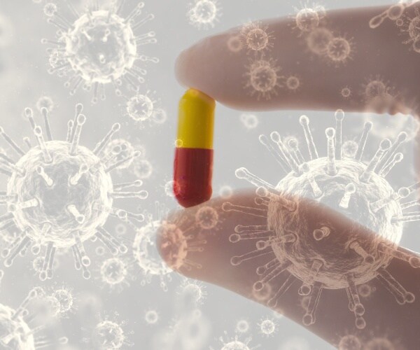 close-up of fingers holding a pill with illustration of COVID viruses floating in background