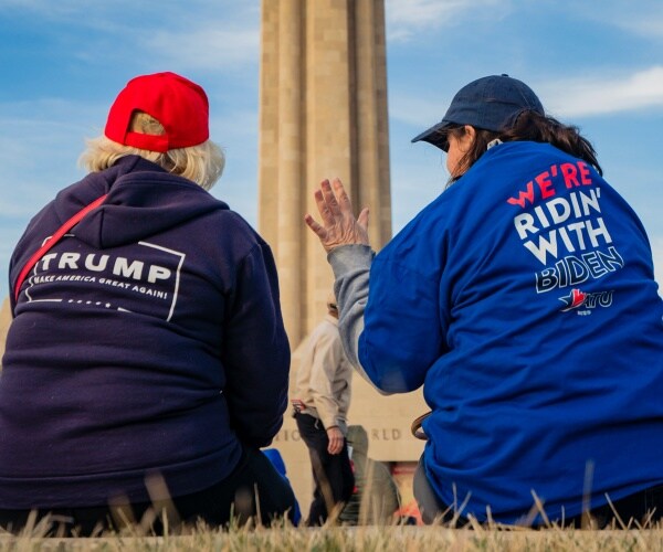 trump supporter in a trump hoodie and red hat speaks with a woman wearing a biden tshirt