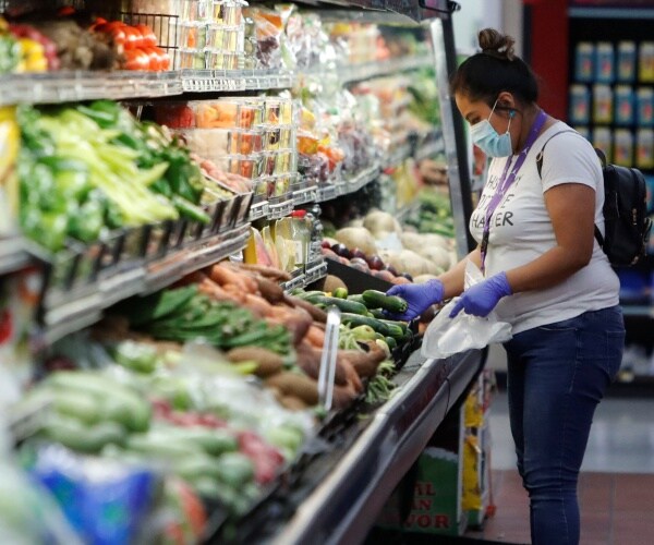 woman wears a mask and gloves and shops in the produce section of the grocery store