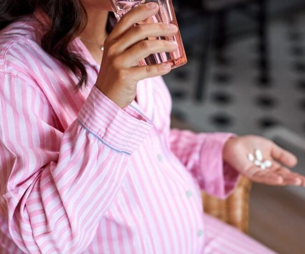 pregnant woman in pajamas with pills, glass of water in her hands