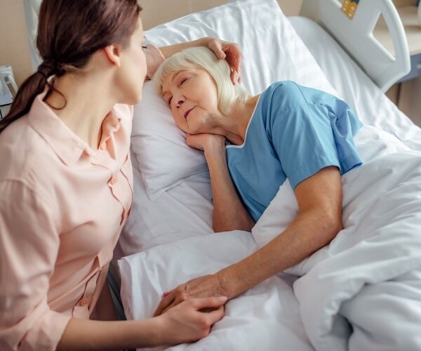 young woman comforting older woman in hospital bed