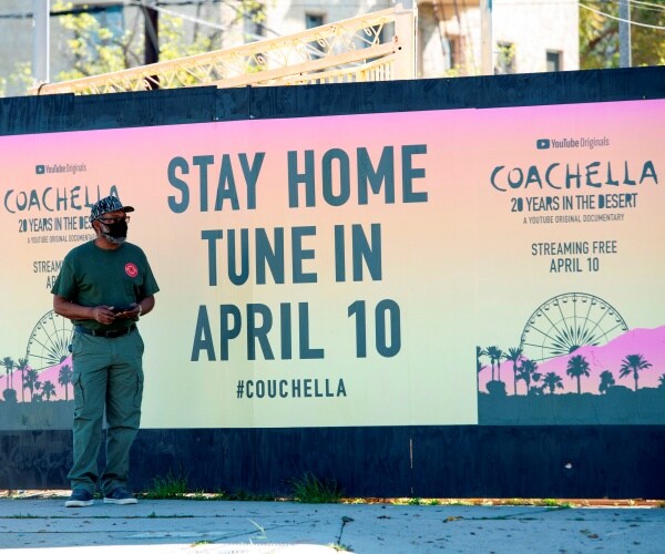 man stands in front of pink, orange, and yellow coachella poster