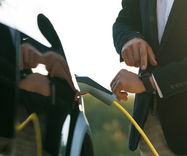 an electric vehicle charges while the driver checks his watch
