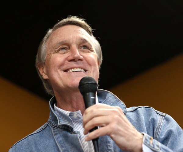 perdue in a striped shirt and denim jacket speaking into a mic