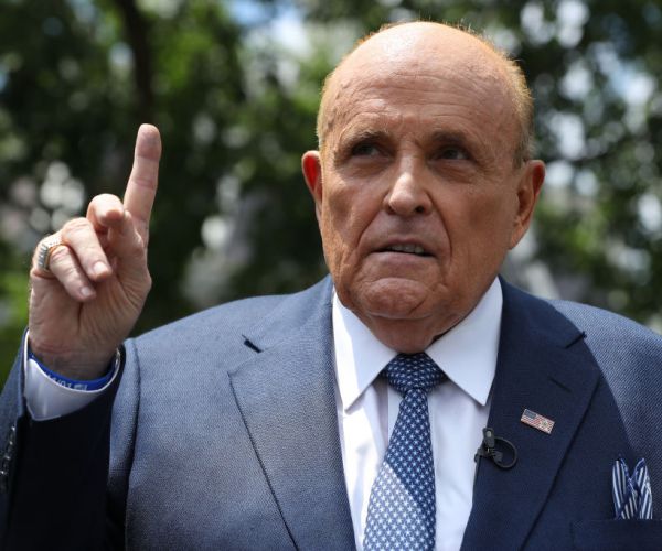 giuliani in a suit and polka dotted tie standing outside pointing his finger up to the sky