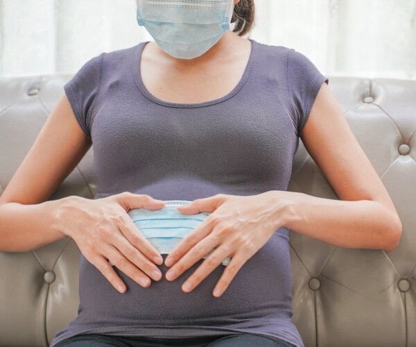 Pregnant woman sitting on couch with a mask on and over her pregnant belly