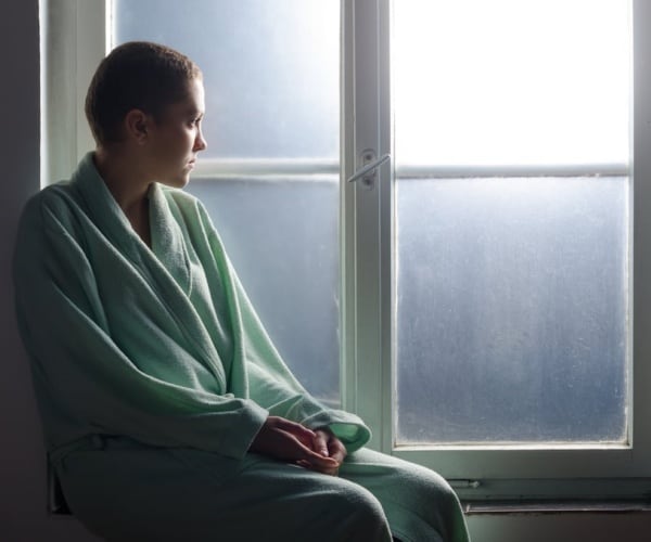 young woman who lost hair in robe looking out window
