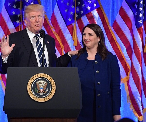 president donald trump and ronna mcdaniel stand in front of flags while the president speaks