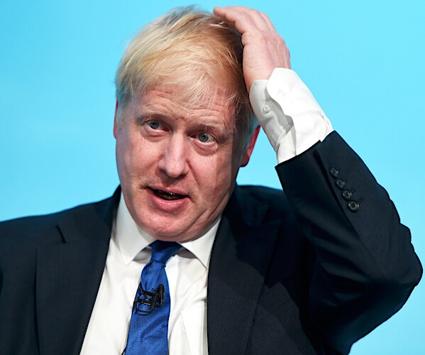 boris johnson scratches his top back of his head with his left hand as if he is confused