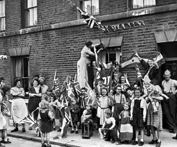 men women and children holding uk flags and celebrating in the streets