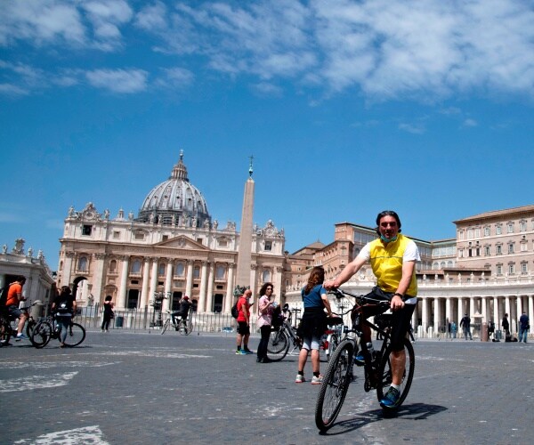 man on a bicycle wearing yellow and others in the background in st peter's square