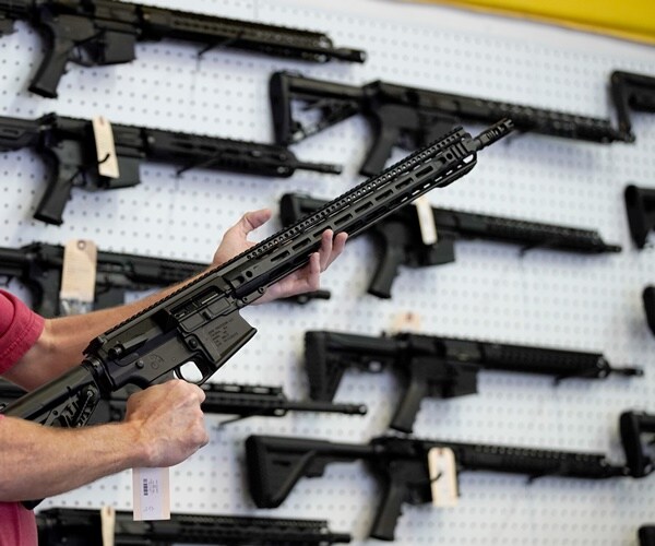 a man holds up an ar-15 to examine in a gun shop