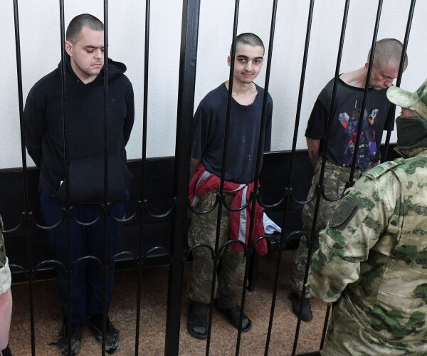 three men in a holding cell surrounded by soldiers