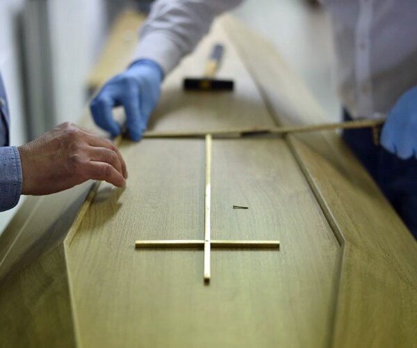 a christian cross is placed on the coffin of a covid-19 victim