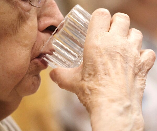 an elderly woman sips a glass of water after taking her medicine