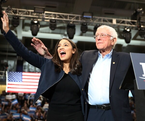 aoc in a black dress and blue jacket with sanders in navy blue pants black jacket and light blue shirt
