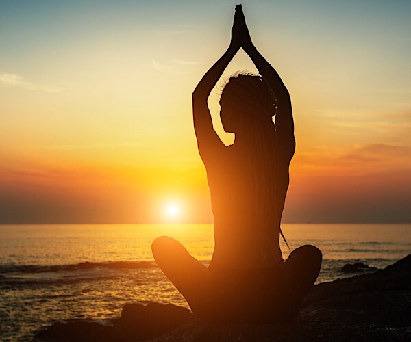 a woman does namaste on the beach before a beautiful sunrise