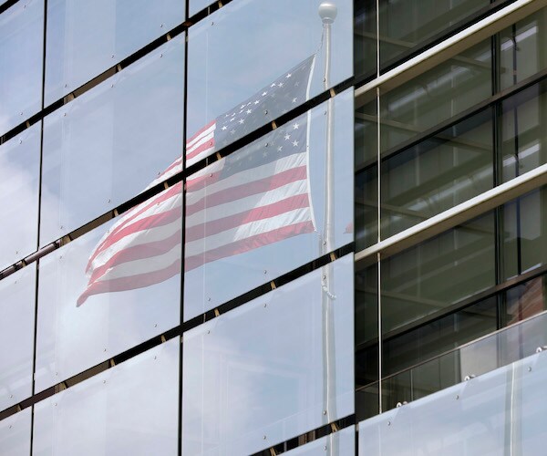 an american flag waves in reflect of the window of one of the freedom towers in new york city