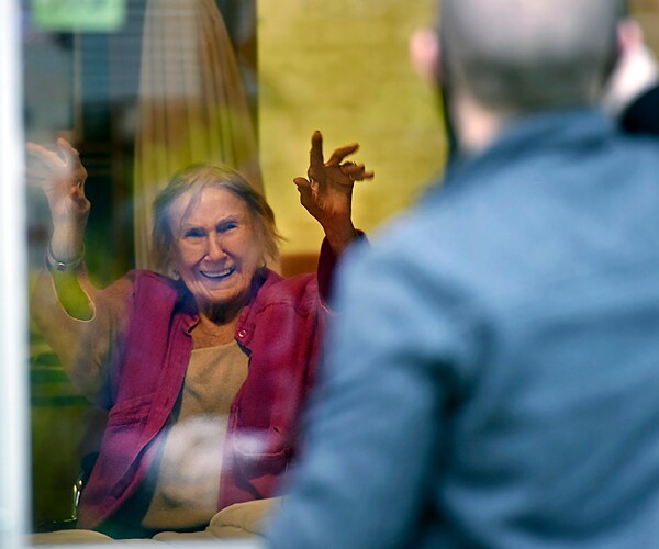 a man waves to an elderly woman through the window of an illinois nursing home
