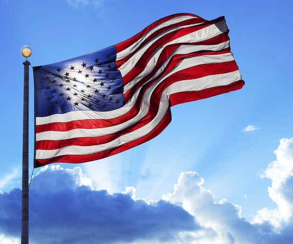 american flag against a partly cloudy sky with sun shining through it