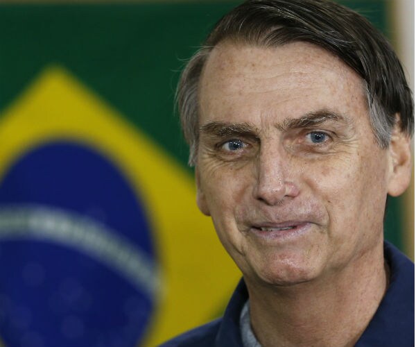 Jair Bolsonaro stands in front of a flag