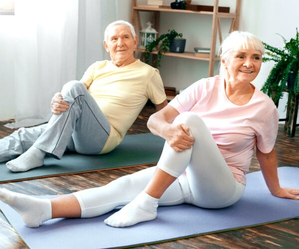 a man and a woman sit on yoga mats in a bent-knee stretch