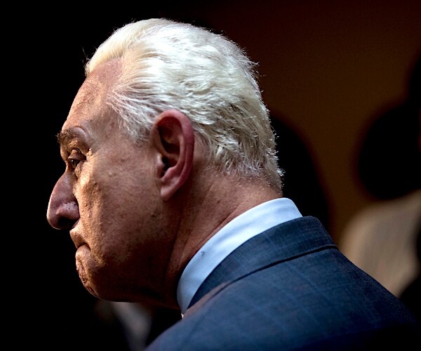 roger stone stands quietly in a court room looking to the left and listening