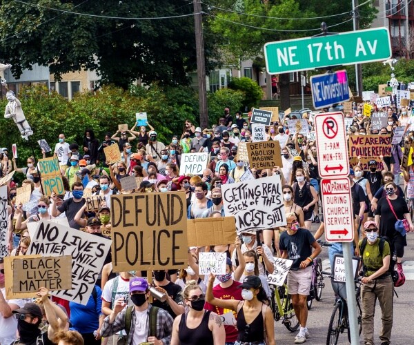 protesters in a large crowd, some wearing masks, hold up signs in support of blm and defunding police