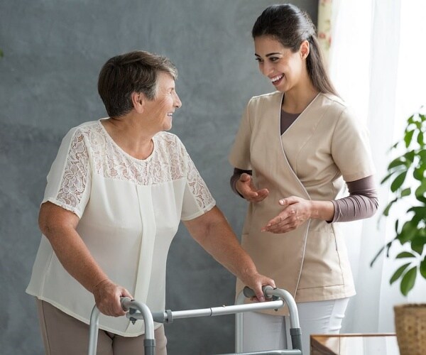 older woman using walker talking to a healthcare worker