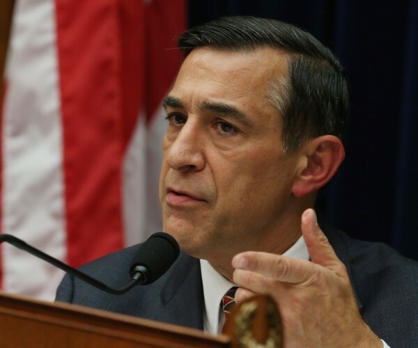 issa in a suit speaking at a podium with a us flag next to him