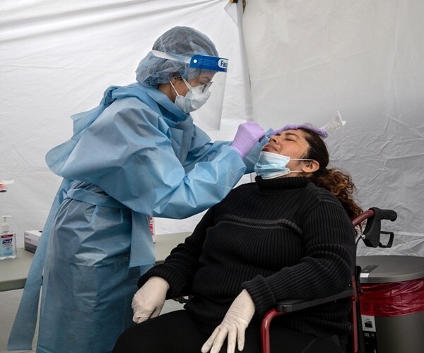 a nurse in a surgical gown and mask uses a nasal swab to test a woman for coronavirus