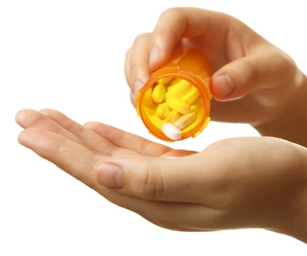 woman pours prescription drug tablets into her hand from an orange container