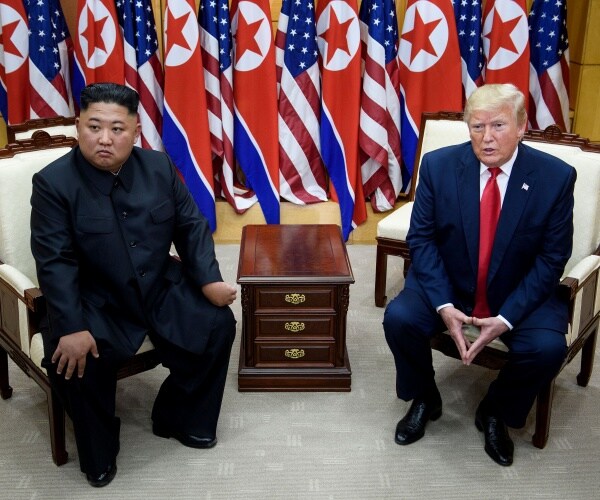 trump and kim jong un sitting down in chairs in front of nk and american flags