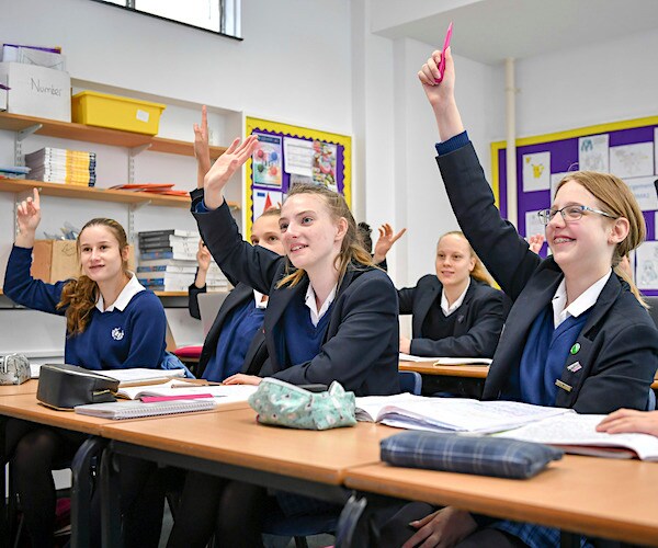 school girls sit with right hands raised to be called on to answer a teacher's question