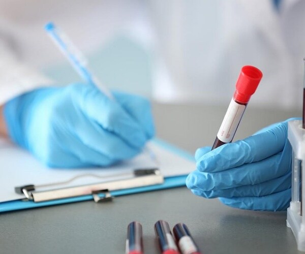 lab technician holding a blood sample and writing in a log
